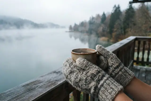 Handpflege im Winter: Hände in Fäustlingen halten eine dampfende Tasse am Balkon