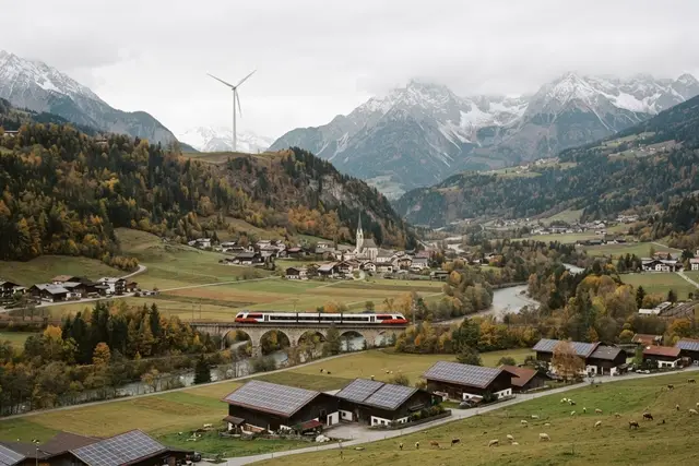 Klimagesetz Österreich: Alpental mit Windrad, Solardächern und Bahn im Herbst